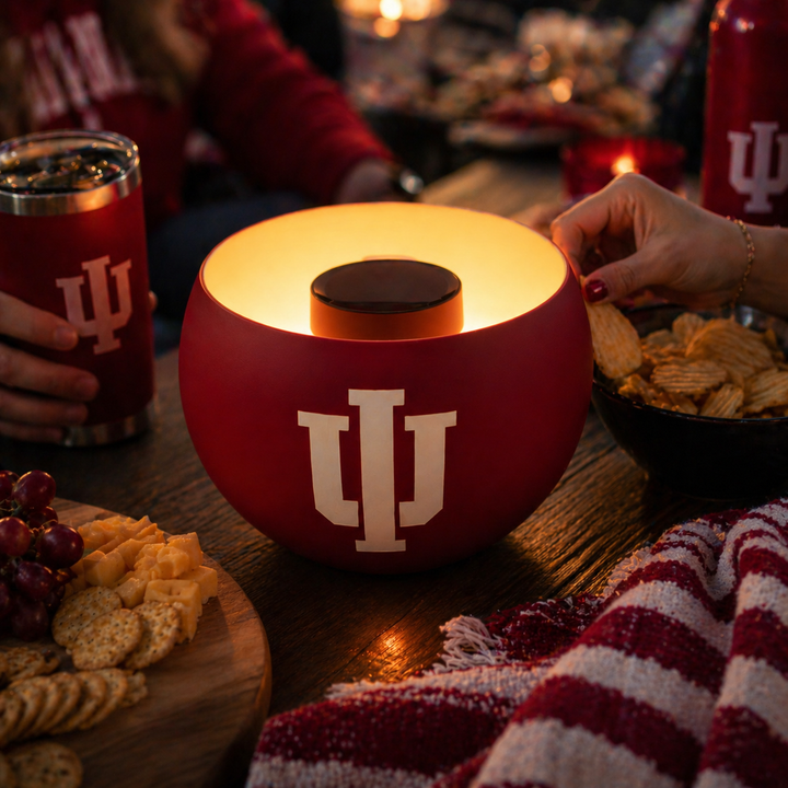 Red solar fire bowl light with Indiana University logo on a table with people and snacks.