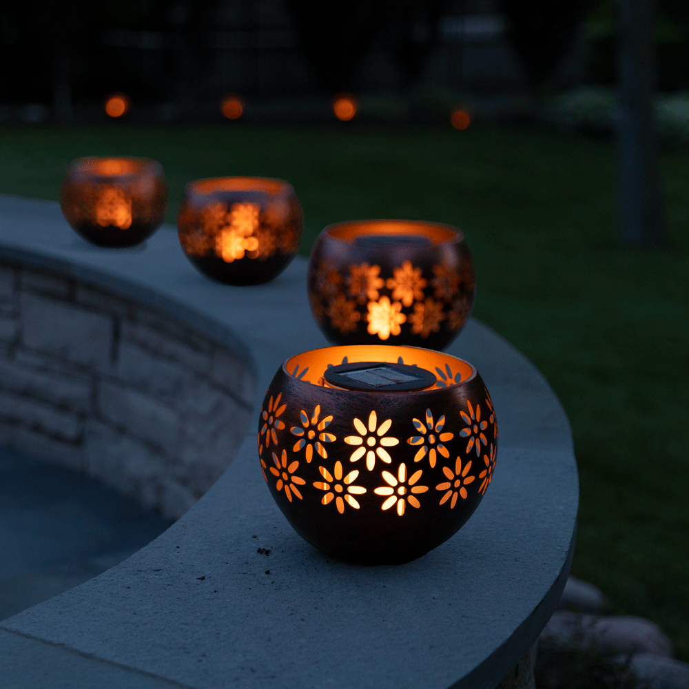 Decorative solar lanterns with floral patterns on a stone ledge at night.